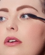 Close-up image of someone looking to the side of the camera and applying a mascara wand to their eyelashes
