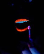 person applying neon orange liquid lipstick in the dark