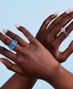 Picture of two hands with long, light pink acrylic nails and colorful rings against a blue background