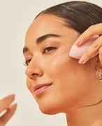 Photo of a young person using a makeup blending sponge to apply foundation while looking into a compact mirror.