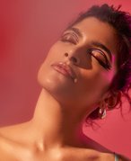 Image of a person with their head tilting up and brunette hair, looking up with eyes closed. The background is red.