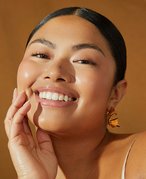 Close-up picture of a model smiling at the camera with their hand on their chin