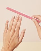 Close-up of person's hands holding a pink nail file to one hand