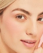 Person with a blonde pixie cut looks at the camera and touches their fingertips to their temple