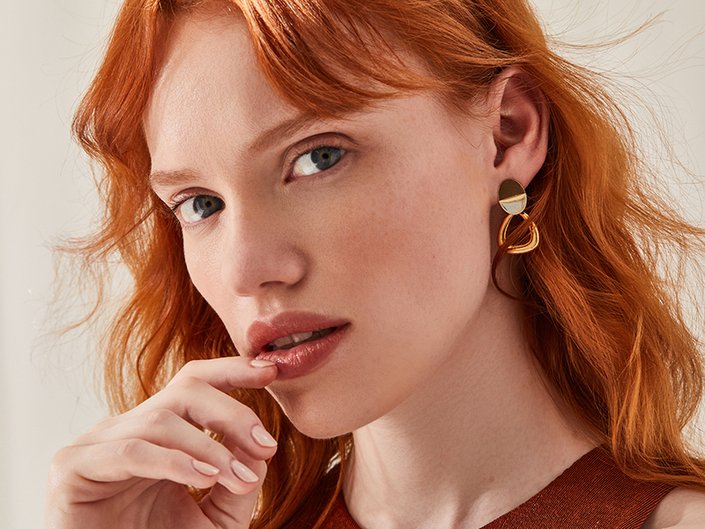 Person with red hair looking at the camera and touching their lips