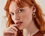 Person with red hair looking at the camera and touching their lips