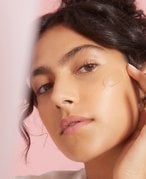 person with dark hair touching their finger to their cheek