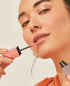 Person with dark hair applying lipstick to their lips